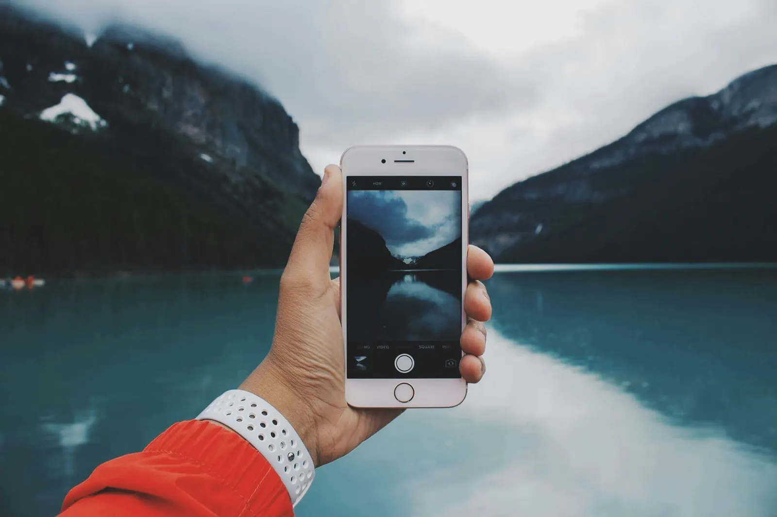 A hand holding up a phone to photograph a mountain lake.